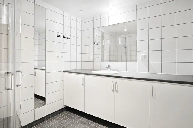 Badet har en innredning med plass til oppbevaring, veggmontert toalett og dusjhjørne.