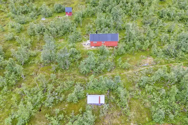 Oversikt hytta med rød sjå og utedo til venstre. Båthus helt til høyre.